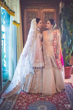 two women standing next to each other in front of a door wearing wedding dresses and veils