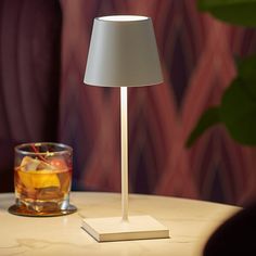 a table lamp sitting on top of a white table next to a glass filled with liquid