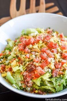 a white bowl filled with lettuce, tomatoes and other toppings on top of it