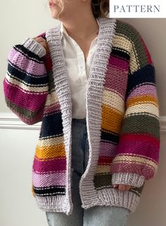 a woman wearing a multicolored cardigan standing against a wall with her hands on her hips