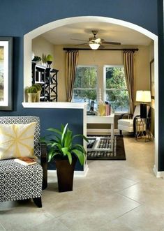 a living room filled with furniture and paintings on the wall next to a doorway that leads to a kitchen