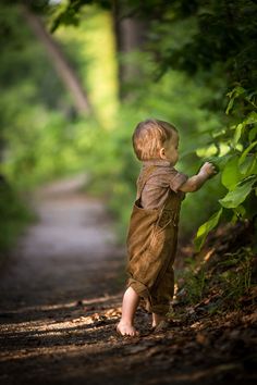 a little boy walking down a dirt road next to a lush green tree filled forest