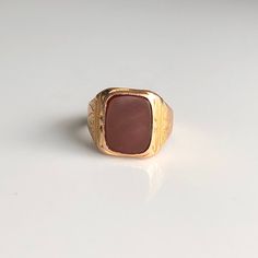 A vintage 15 carat rose gold signet ring displaying a carnelian stone. The gold has a heavy look about it and has lovely engraved detailing. CONDITION: Wear consistent with age and use. Please see photos for more detail. HALLMARKED 15 CARAT GOLD  RING SIZE: UK: O 1/2 | US: 7 1/4 BAND WIDTH (NARROWEST): 4mm STONE FACE: 10mm x 14mm WEIGHT: 7.0 grams (DDZ) Luxury Red Carnelian Signet Ring, Classic Carnelian Signet Ring For Formal Occasions, Classic Carnelian Signet Ring For Formal Events, Classic Gold Rectangular Ruby Ring, Classic Rectangular Ruby Ring In Gold, Classic Gold Ruby Ring With Rectangular Shape, Classic Brown Signet Ring For Anniversary, Classic Carnelian Signet Ring With Polished Finish, Classic Carnelian Signet Ring For Anniversary