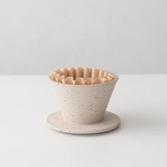 a white cup sitting on top of a saucer filled with wooden spoons in front of a gray wall