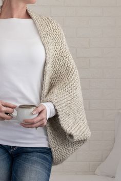 a woman is holding a cup in her hand and wearing a sweater over her shoulders