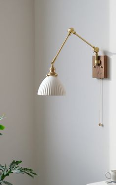 a white lamp on the wall next to a potted plant