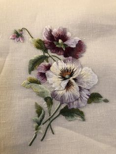 an embroidered flower on a white cloth with green leaves and purple flowers in the center