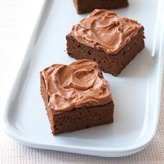 three pieces of brownie with chocolate frosting sitting on a white plate next to each other