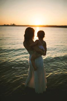 two women are standing in the water with their arms around each other as the sun sets