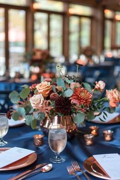 an elegant centerpiece with flowers and greenery sits on a blue table cloth at the reception