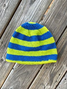 a blue and yellow striped knitted hat sitting on top of a wooden fence next to a piece of wood