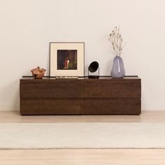 a wooden dresser with two vases and a painting on the wall behind it in an empty room