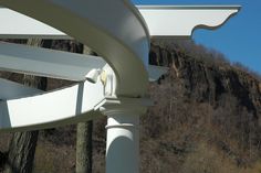 the corner of a white metal structure in front of a mountain side with trees and bushes