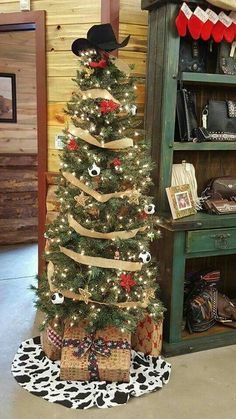 a decorated christmas tree in the corner of a room next to a book shelf with cowboy hats on it