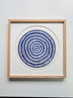 a blue and white circular artwork mounted on a wall above a wooden framed object in a wood frame