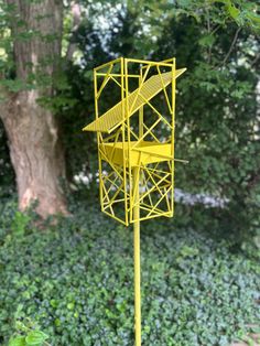 a yellow metal structure sitting on top of a lush green field next to a tree