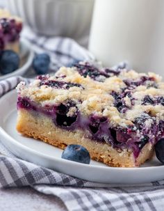 a piece of blueberry crumb bars on a white plate next to a glass of milk