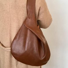 a person holding a brown leather purse on their back shoulder and wearing a tan sweater