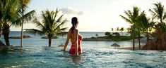 a woman standing in the middle of a swimming pool next to palm trees and water