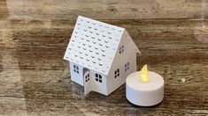 a small white house with a lit candle in front of it on a wooden table