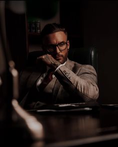 a man sitting at a desk in front of a laptop computer wearing glasses and a suit