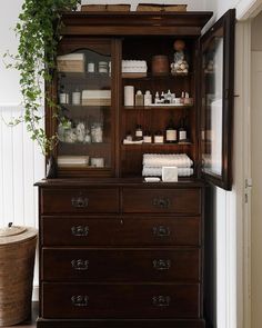 a wooden cabinet with lots of bottles and towels on it's shelves next to a wicker basket