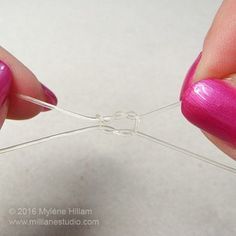 someone is working on some wire with pink nail polish and purple nails, while another hand holds the string