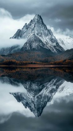 the mountains are covered in clouds and trees, while the water is still reflecting them