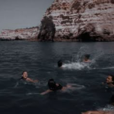 several people swimming in the water near some cliffs