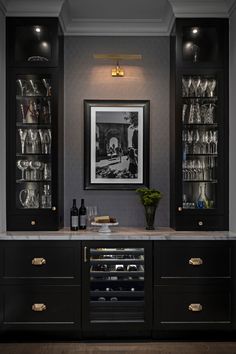 a black cabinet with wine glasses and bottles on it in front of a framed photograph