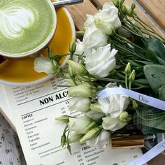 there is a cup of green tea next to some white flowers and a paper with writing on it