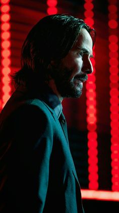 a man with long hair and beard standing in front of bright red lights, looking off to the side