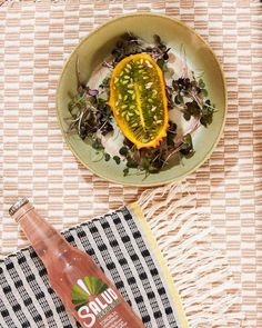 a bowl of salad and a bottle of juice on a tablecloth with a napkin