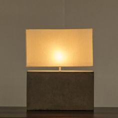 a lamp that is sitting on top of a wooden table in front of a gray wall