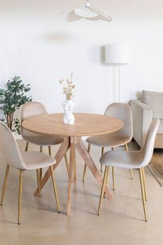 a round wooden table surrounded by beige chairs and a white vase with flowers on it