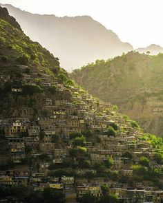 a hillside covered in lots of houses on top of a lush green hill side next to mountains