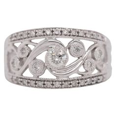 This Vintage Round Cut Diamond Ring set in 14 Karat white gold dates back to the 1980's and has such a beautiful and notable design. The center stone is Round Brilliant Cut weighing 0.22 ct, H in color, SI2-I1 in clarity and there are 32 round brilliant cut side diamonds weighing 0.48 carats. The diamonds are all encased in beautiful swirls and filigree of 14K white gold. Item Details: Ring Size: 10 Metal Type: 14K White Gold Weight: 6.1 grams Hallmarks: 14K Engraving: none Width: 12.5 mm at head tapering to 1.6 mm at bottom of the shank Finger to Top of Ring: 5.3 mm Center Stones: Type: Diamond Count: 1 Shape: Round Brilliant Cut Carat Weight: 0.22CT Color: H Clarity: SI2-I1 Accent Stones (32): Cut: Round Carat Weight: 0.48 CT Color: H-I Clarity: SI1-SI2 Round Diamond Ring Set, Round Diamond Ring Settings, Round Cut Diamond Ring, Diamond Ring Set, Round Diamond Ring, Diamond Ring Settings, Three Stone Rings, Three Stone, Round Cut Diamond