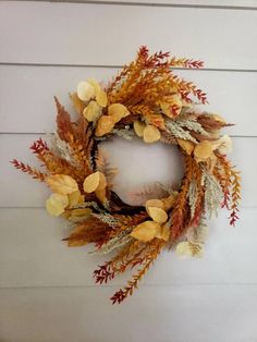 a wreath is hanging on the side of a wall with autumn leaves and dried flowers