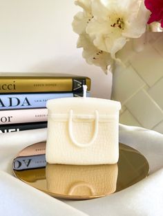 a small white bag sitting on top of a plate next to some books and a vase with flowers