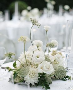 white flowers and greenery are arranged on the table