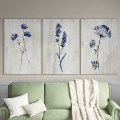 three blue and white flowers are hanging on the wall above a couch in a living room