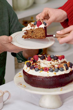 two people are cutting into a cake with berries on it and one person is holding a knife