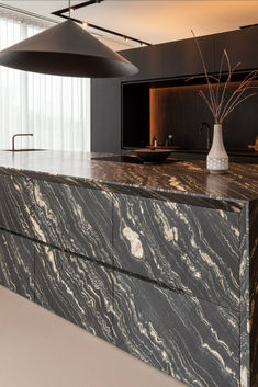 a large kitchen with marble counter tops and black cabinetry, along with two pendant lights