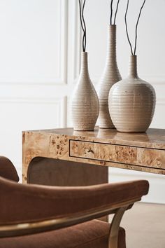 three white vases sitting on top of a wooden table next to a brown chair