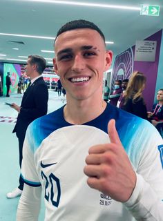 a young man is giving the thumbs up sign in front of his camera while wearing a white and blue shirt