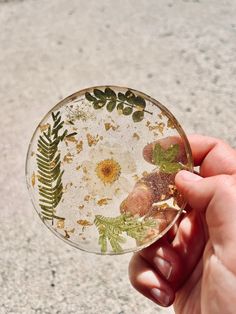 a hand holding a glass plate with flowers and leaves on it