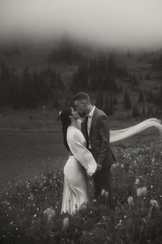 a black and white photo of a bride and groom kissing in the middle of a field