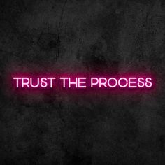 the words trust the process are lit up in pink on a dark background with a neon light