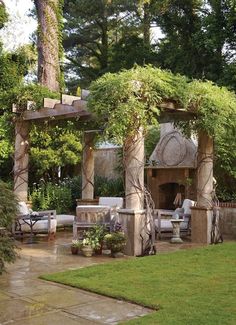 an outdoor fireplace surrounded by greenery in a backyard area with chairs and tables around it