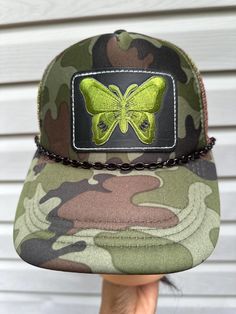 camouflaged trucker hat faux leather patch iron on embroidered butterfly black plastic chain meshed sides and back with extended snap back closure. Summer Adjustable Snapback Hat With Embroidered Patch, Military Style Adjustable Snapback Trucker Hat, Adjustable Trucker Hat With Patches, Adjustable Trucker Hat With Leather Patch For Streetwear, Adjustable Leather Patch Trucker Hat For Streetwear, Adjustable Trucker Hat With Patches And Curved Brim, Summer Adjustable Snapback Hat With Patches, Adjustable Summer Snapback Hat With Patches, Adjustable Trucker Hat With Embroidered Patch